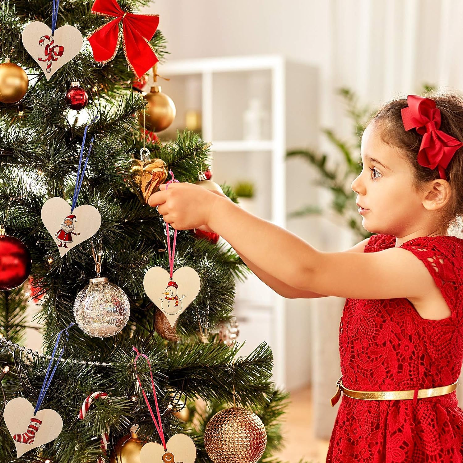 Child in a red dress decorating a Christmas tree with ornaments.