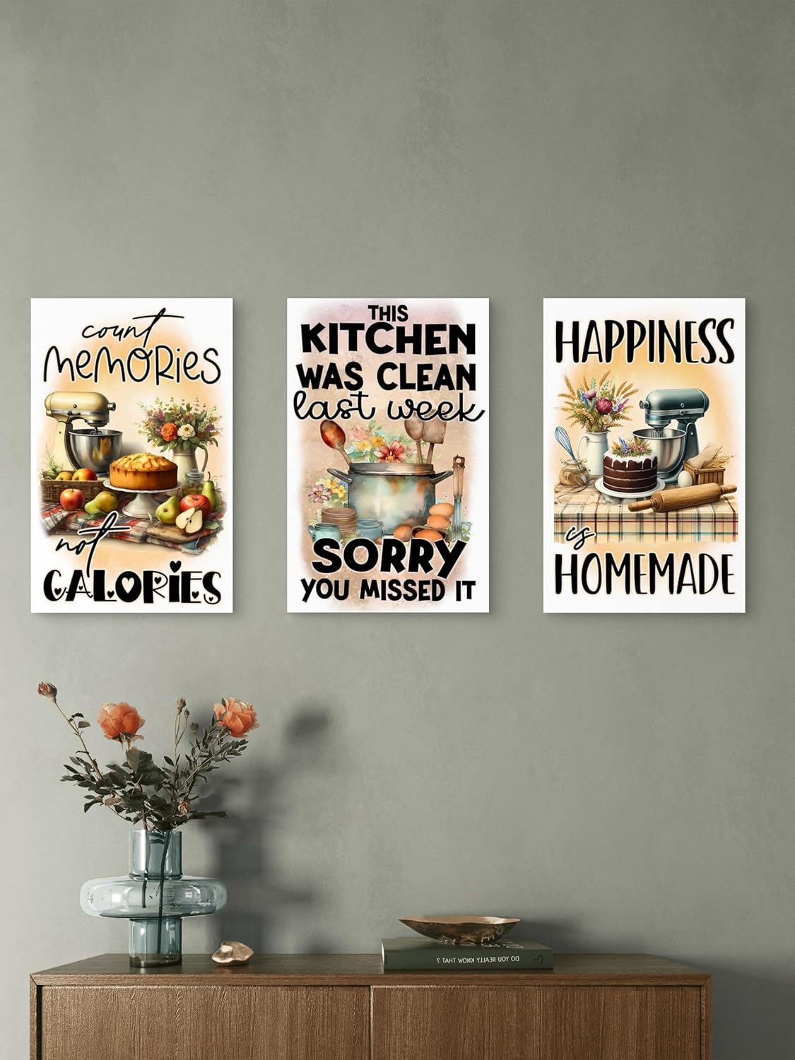 Three kitchen-themed posters on a wall above a wooden cabinet with a vase of flowers.