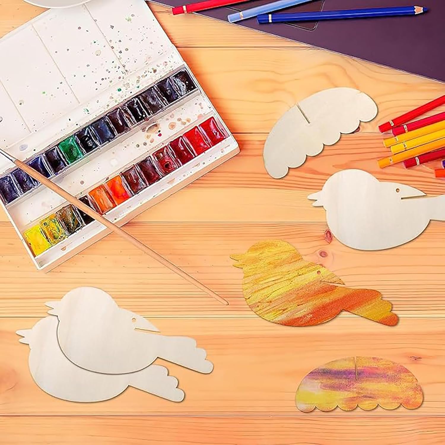 Art supplies including watercolor paints, brushes, and painted animal shapes on a wooden surface.