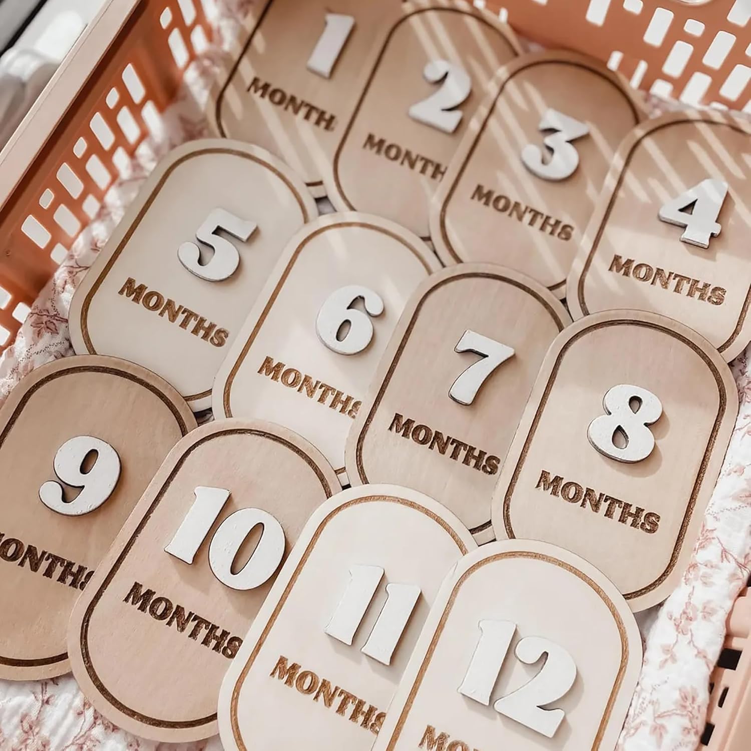 Wooden baby milestone markers with numbers 1 to 12 months on a soft fabric background.