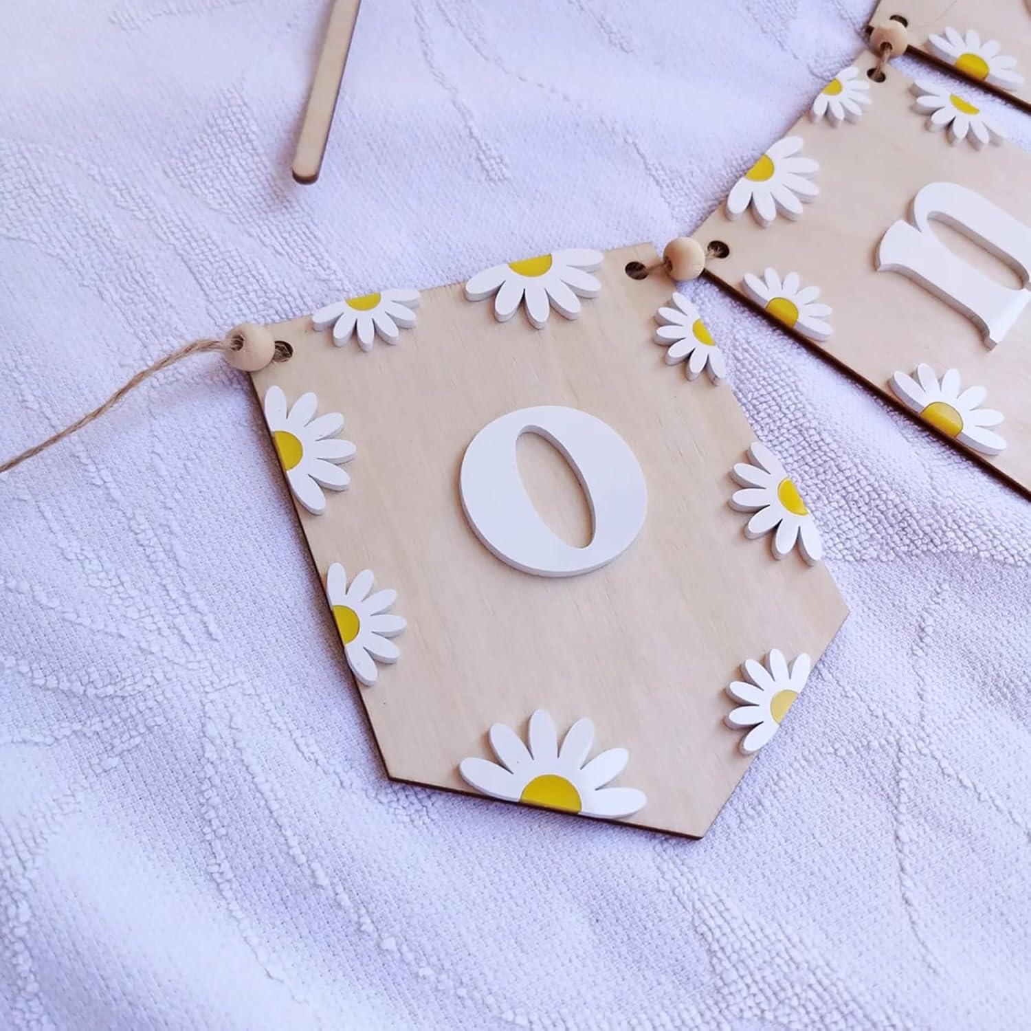 Wooden number '0' with daisy flower decorations on a white fabric background