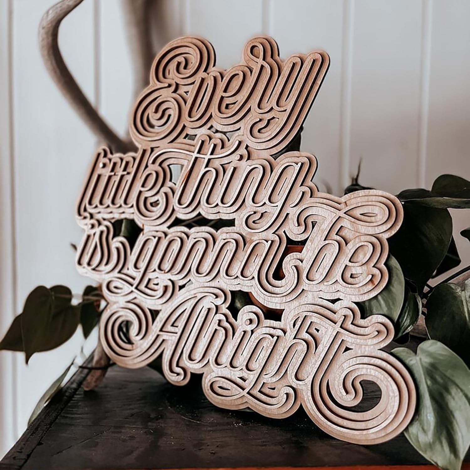 Wooden decorative sign with 'Every little thing is gonna be alright' text on a surface with plants.