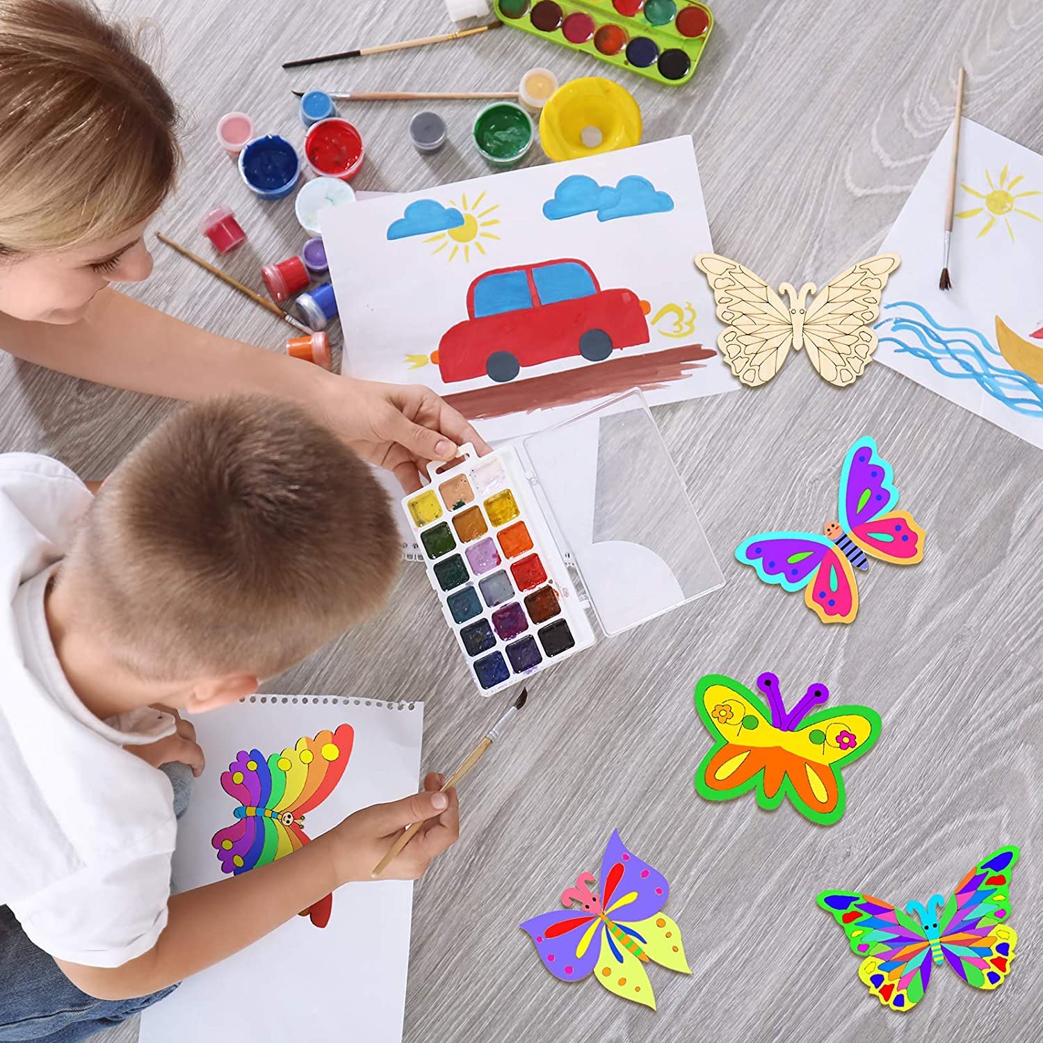 Children painting butterflies and a car with art supplies on a wooden floor.