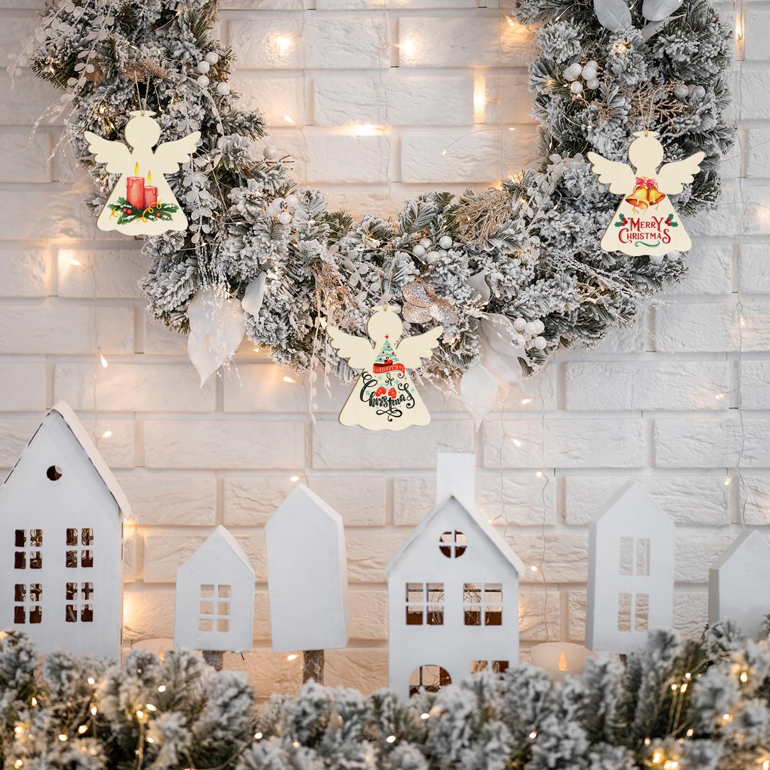 Decorative Christmas scene with wreaths, angel figurines, and small houses against a light brick wall.