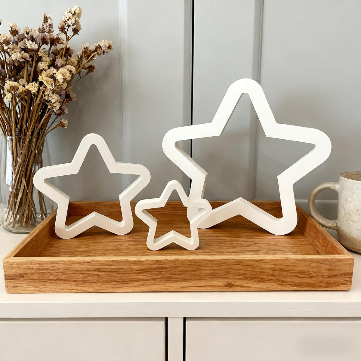 White star-shaped lights on a wooden tray with a vase of dried flowers and a mug in the background.