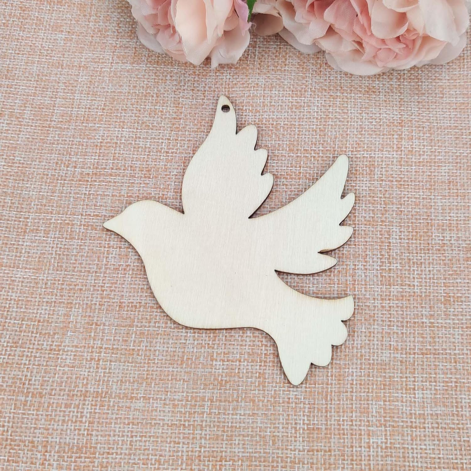Wooden dove-shaped ornament on a textured surface with pink flowers in the background