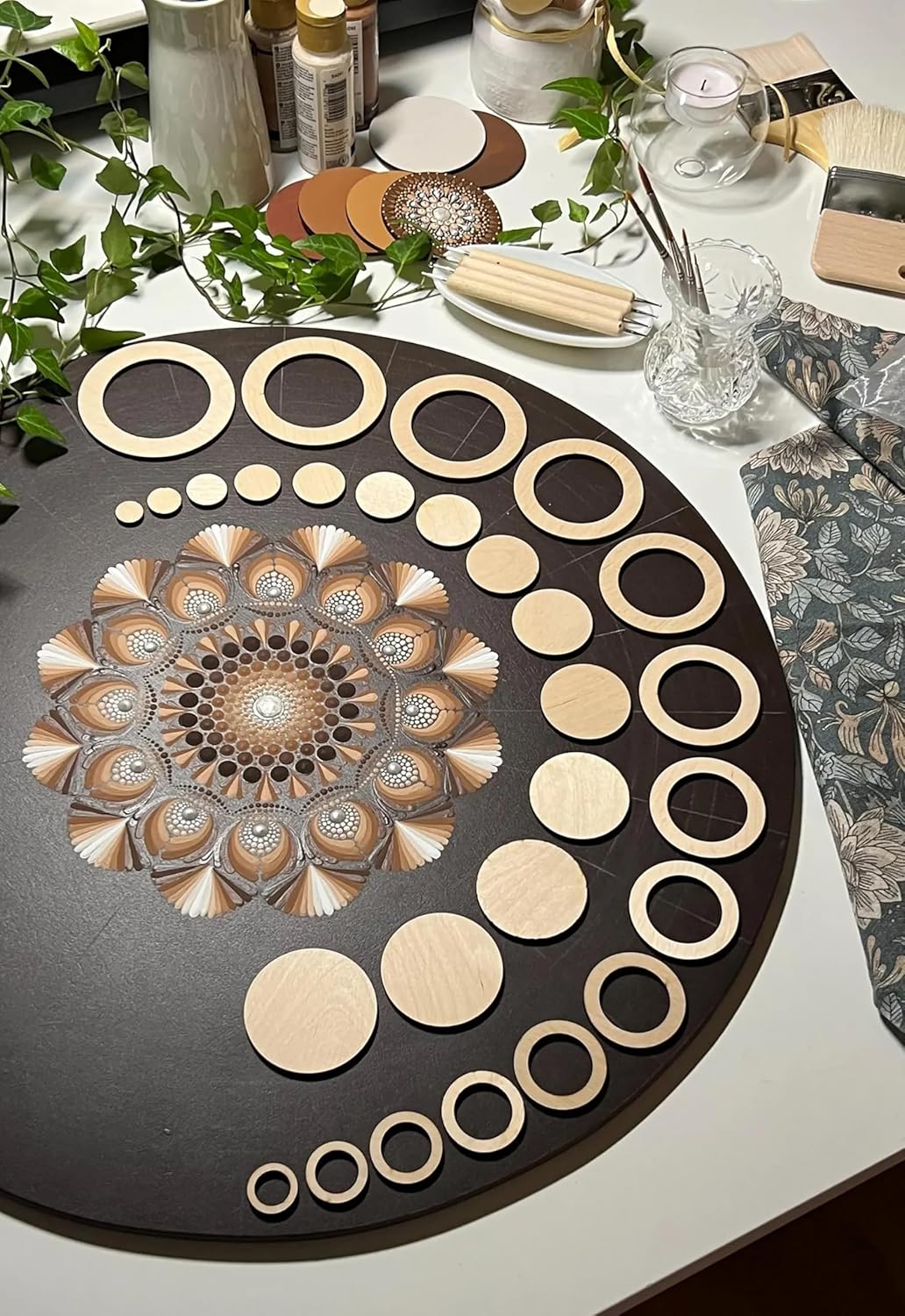 Decorative circular wooden pieces on a black board with a floral design, surrounded by greenery and other decorative items.