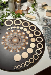 Decorative circular wooden pieces on a black board with a floral design, surrounded by greenery and other decorative items.
