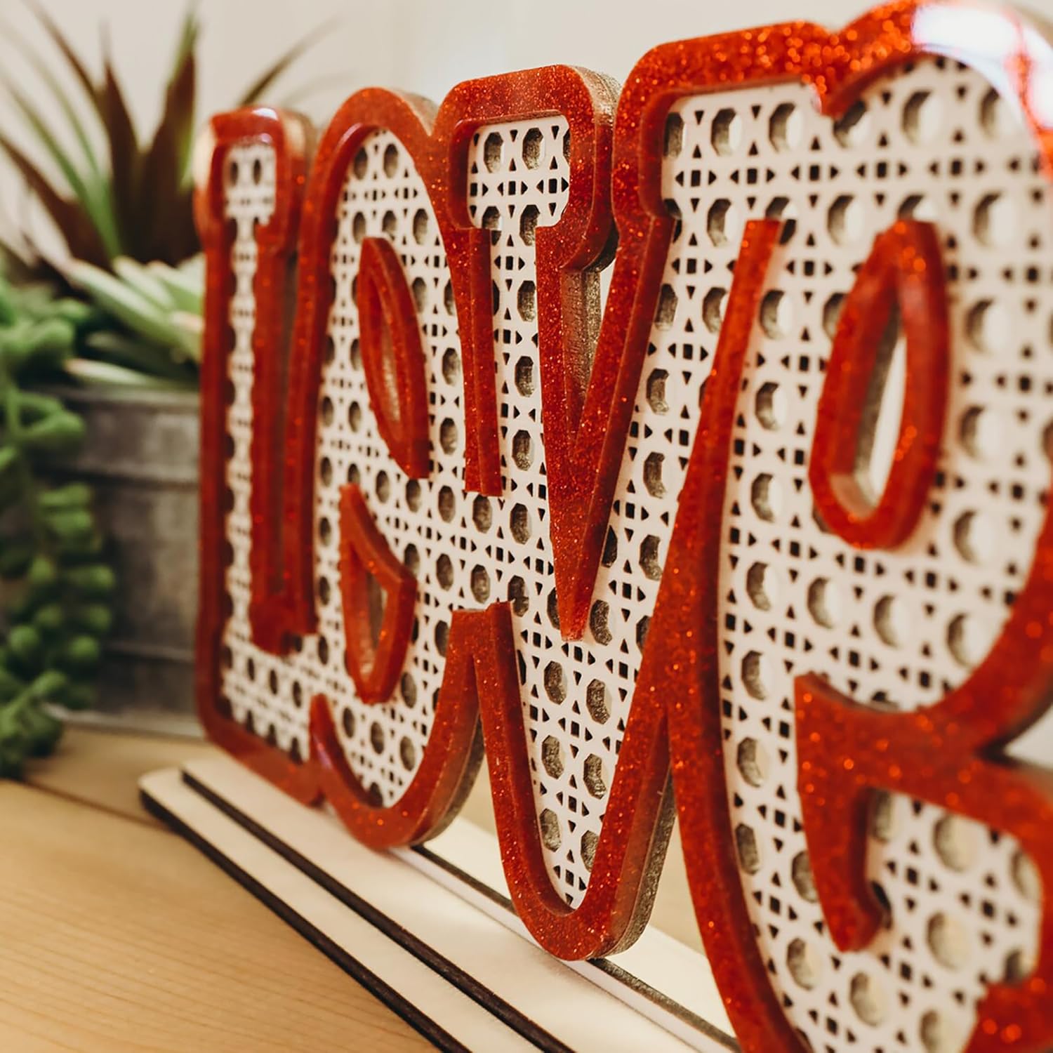 Decorative sign with 'LOVE' on a wooden surface with plants in the background