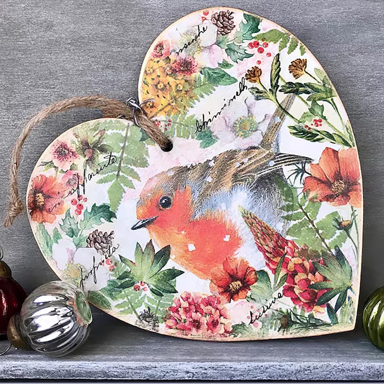 Decorative heart-shaped sign with a robin and floral design on a gray surface.
