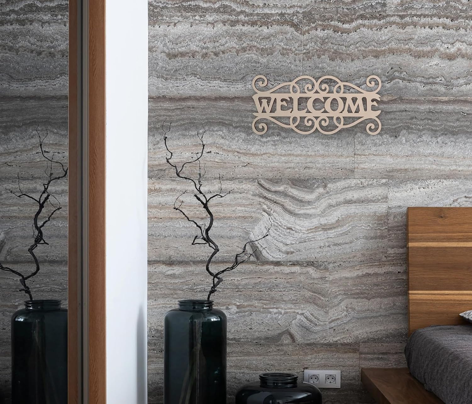 Decorative 'Welcome' sign on a textured wall with vases and a bed in the background.