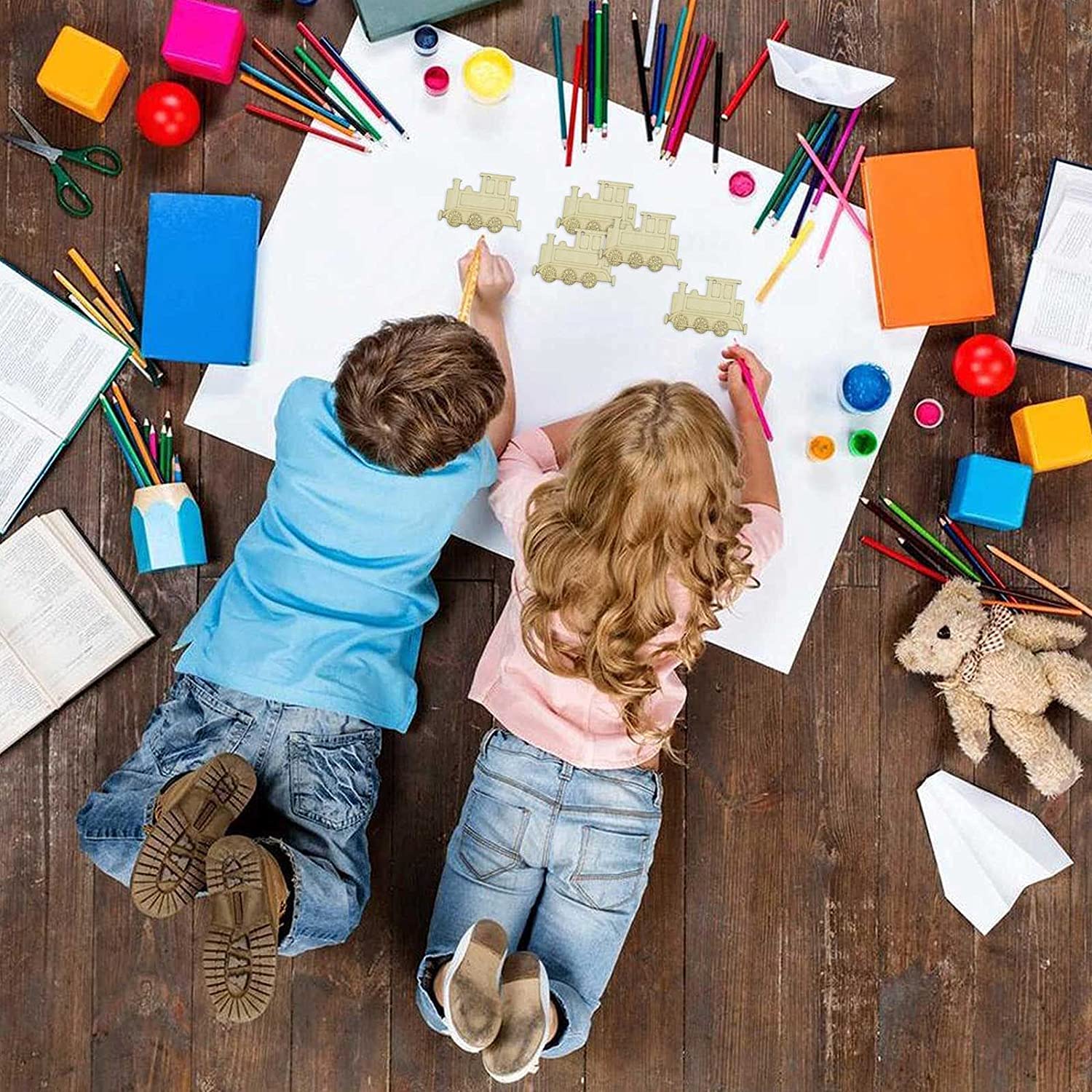 Two children sitting on a wooden floor surrounded by art supplies and toys.