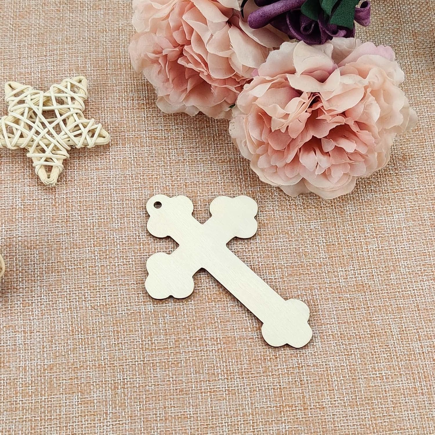 Decorative cross pendant and star-shaped object on a textured surface with pink flowers.