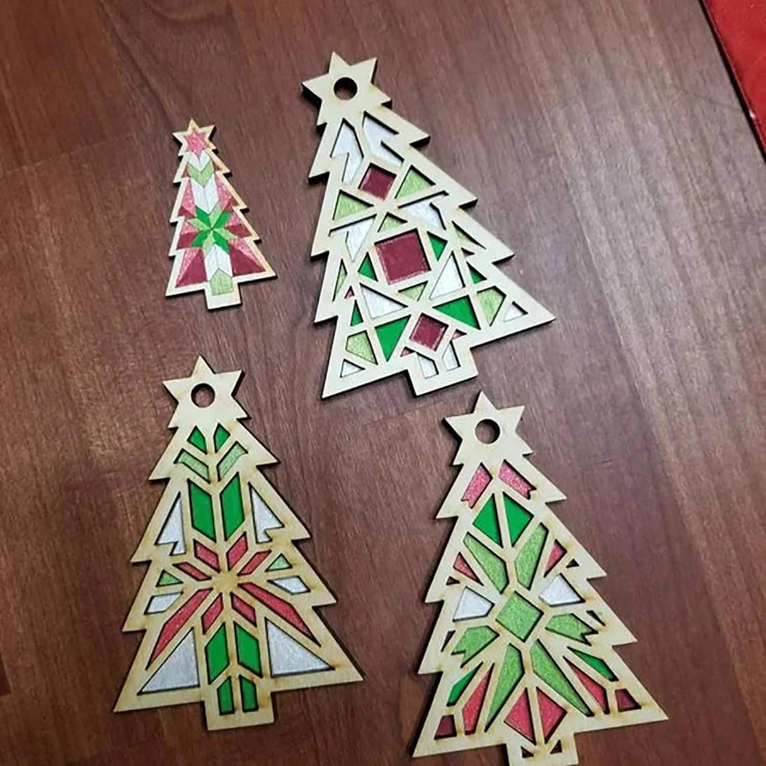 Four geometric Christmas tree ornaments on a wooden surface