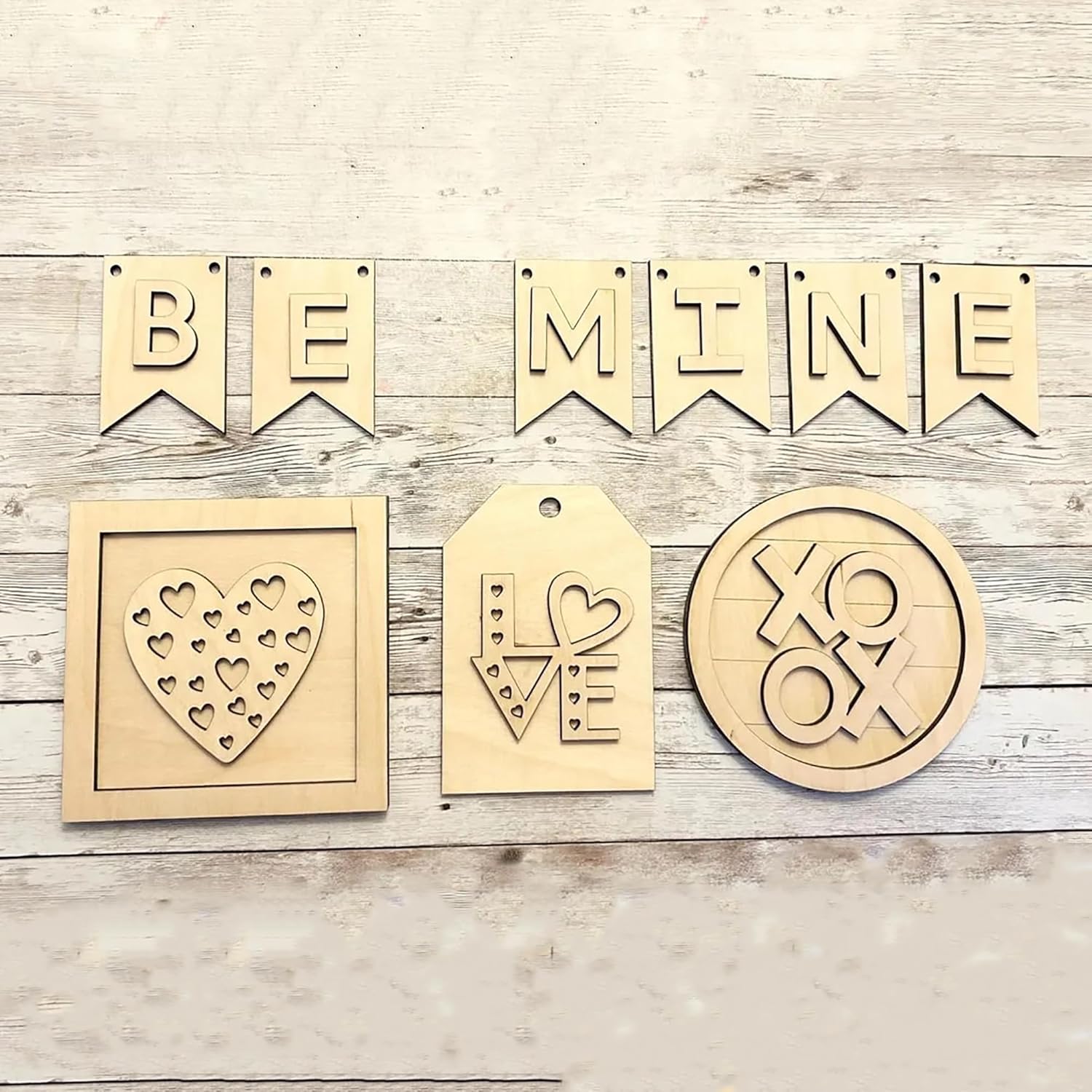 Wooden decorations with 'BE MINE' banner, heart design, 'LOVE' tag, and 'XO' emblem on a wooden surface.