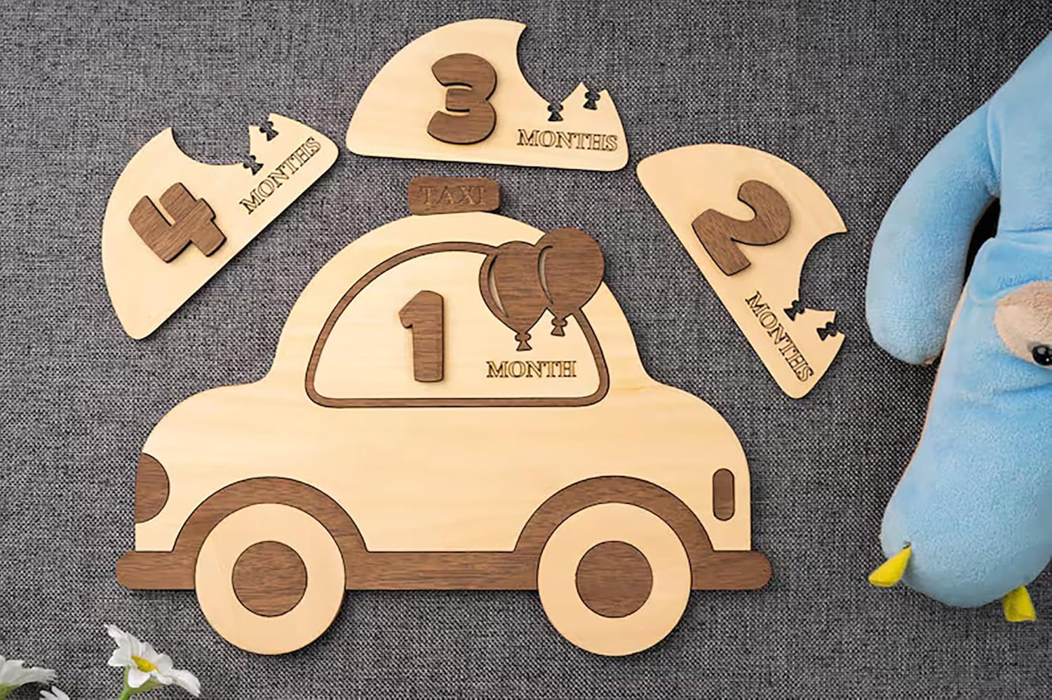 Wooden baby milestone car with detachable months displayed on a textured surface.