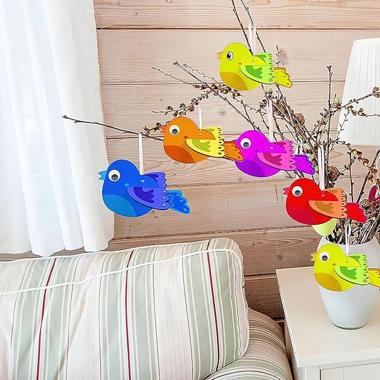 Colorful bird-shaped decorations hanging on a branch indoors.