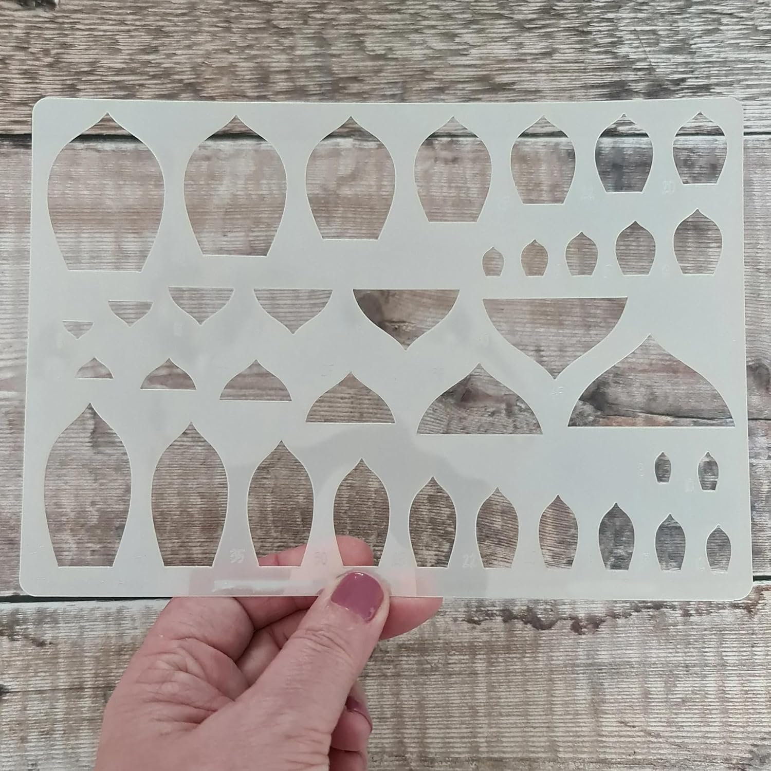 Decorative stencil held by a hand on a wooden surface