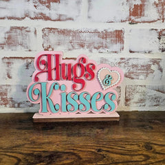 Decorative sign with 'Hugs & Kisses' text on a wooden surface and brick wall background