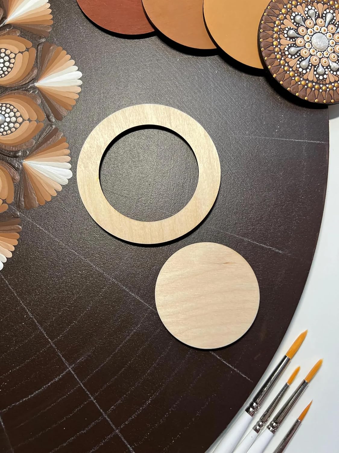 Wooden circular pieces on a dark surface with decorative elements and paintbrushes.