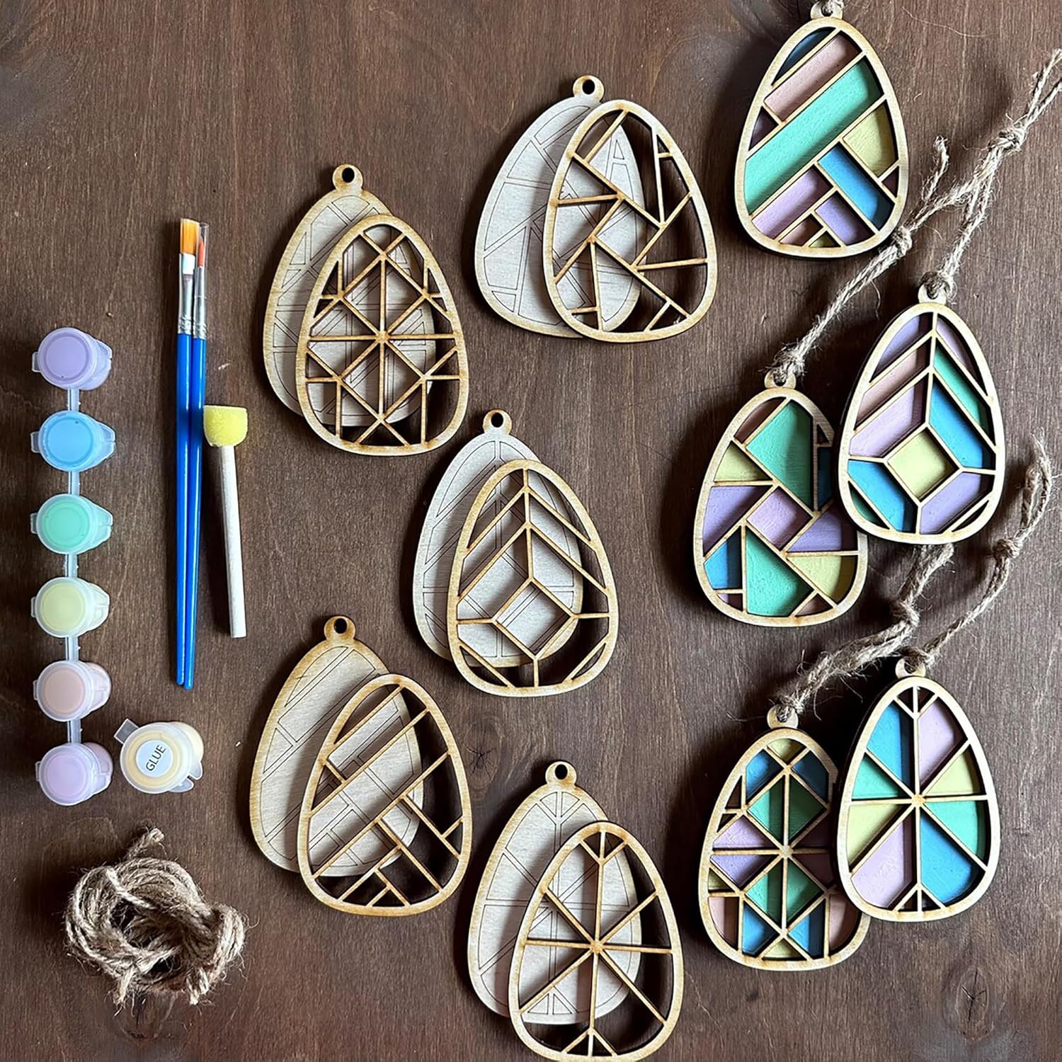 Geometrically patterned teardrop-shaped ceramic decorations on a wooden surface with painting tools.