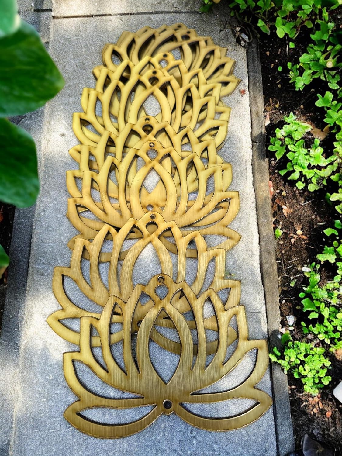 Decorative gold metal artichoke design on a stone surface with green plants around.