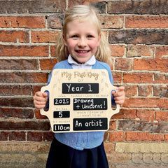 Young girl holding a sign with school information against a brick wall