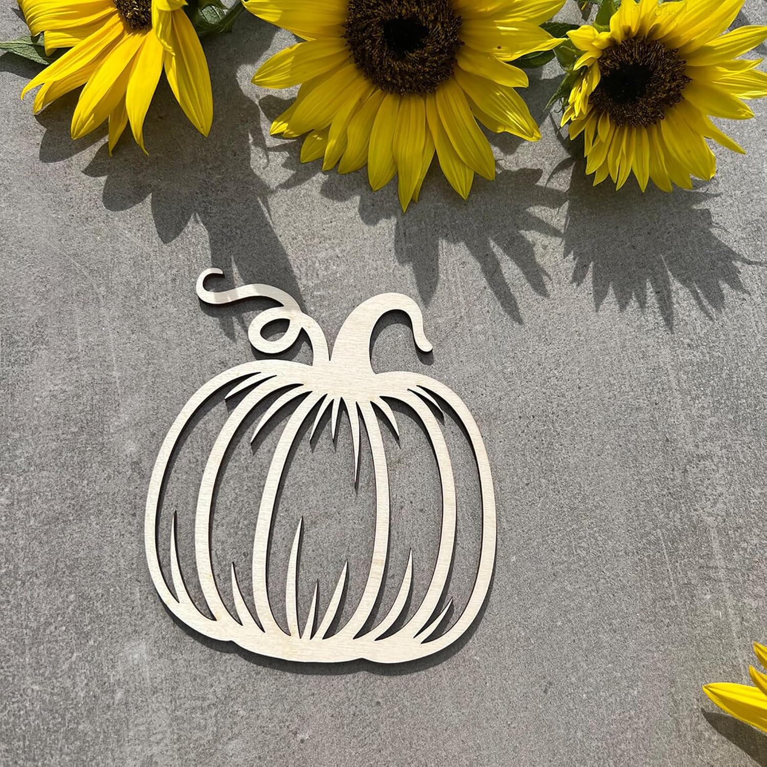 Wooden pumpkin cutout on a gray surface with sunflowers in the background