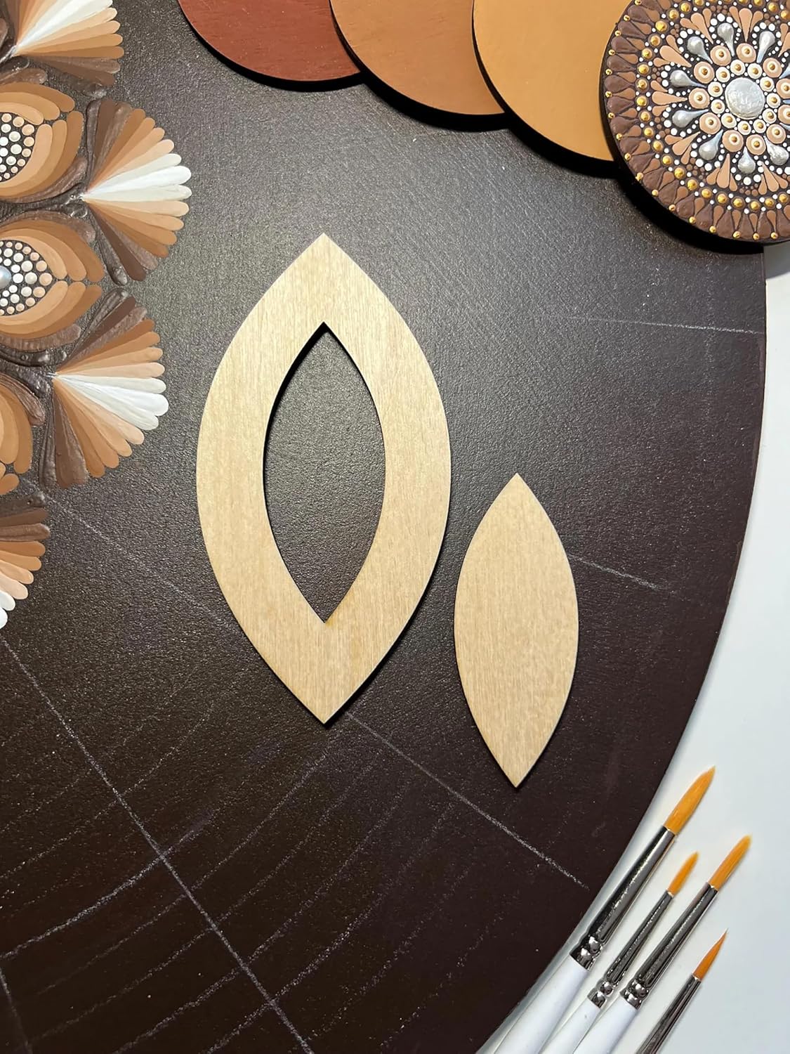 Wooden earring templates on a dark surface with paintbrushes and decorative items.