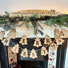 Wooden 'Merry Christmas' banner on a decorated fireplace mantel with greenery and lights.
