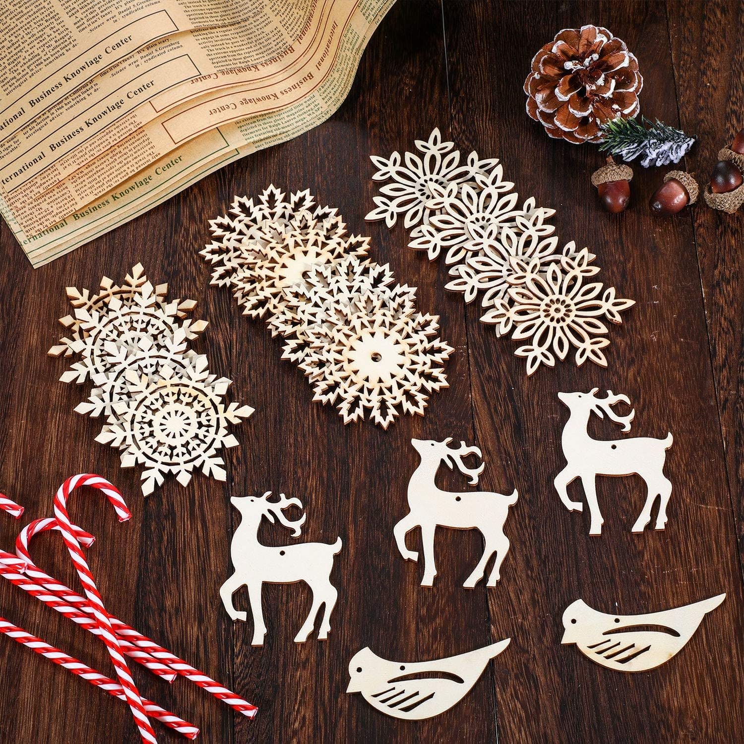 Decorative cutout shapes of snowflakes, reindeer, and birds on a wooden surface with a newspaper and pinecones.