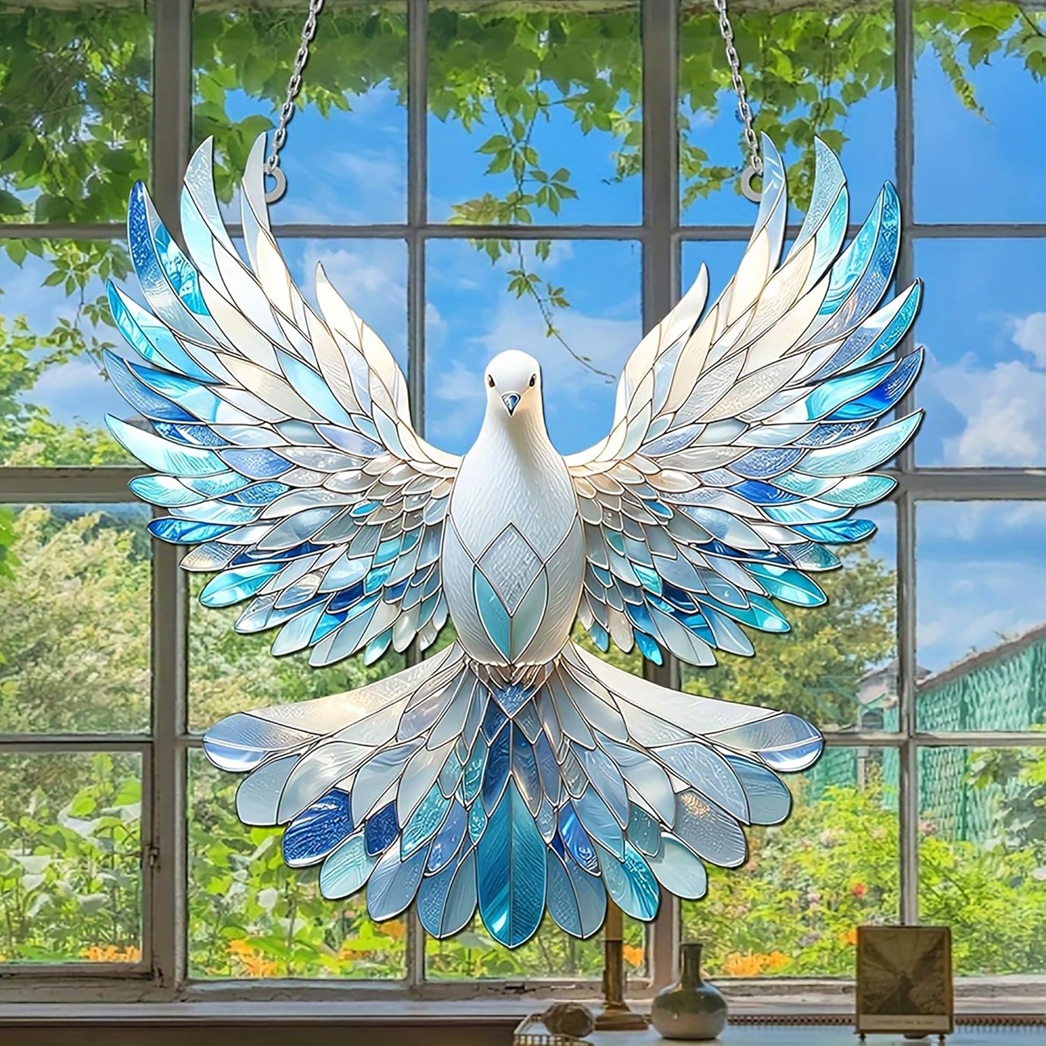 Decorative stained glass dove hanging in front of a window with a view of trees and blue sky.