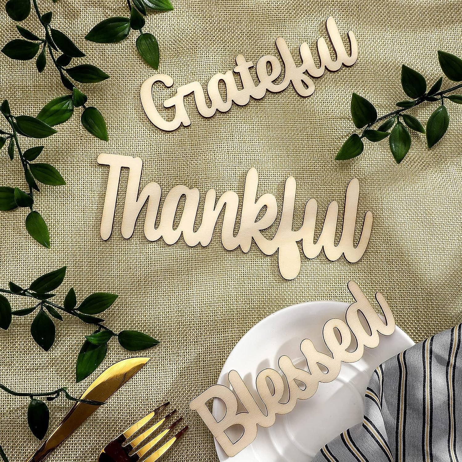 Decorative wooden words 'Grateful', 'Thankful', 'Blessed' on a table setting with cutlery and greenery.