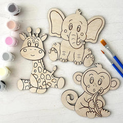 Wooden animal cutouts (giraffe, elephant, monkey) with paint containers and brushes on a light surface