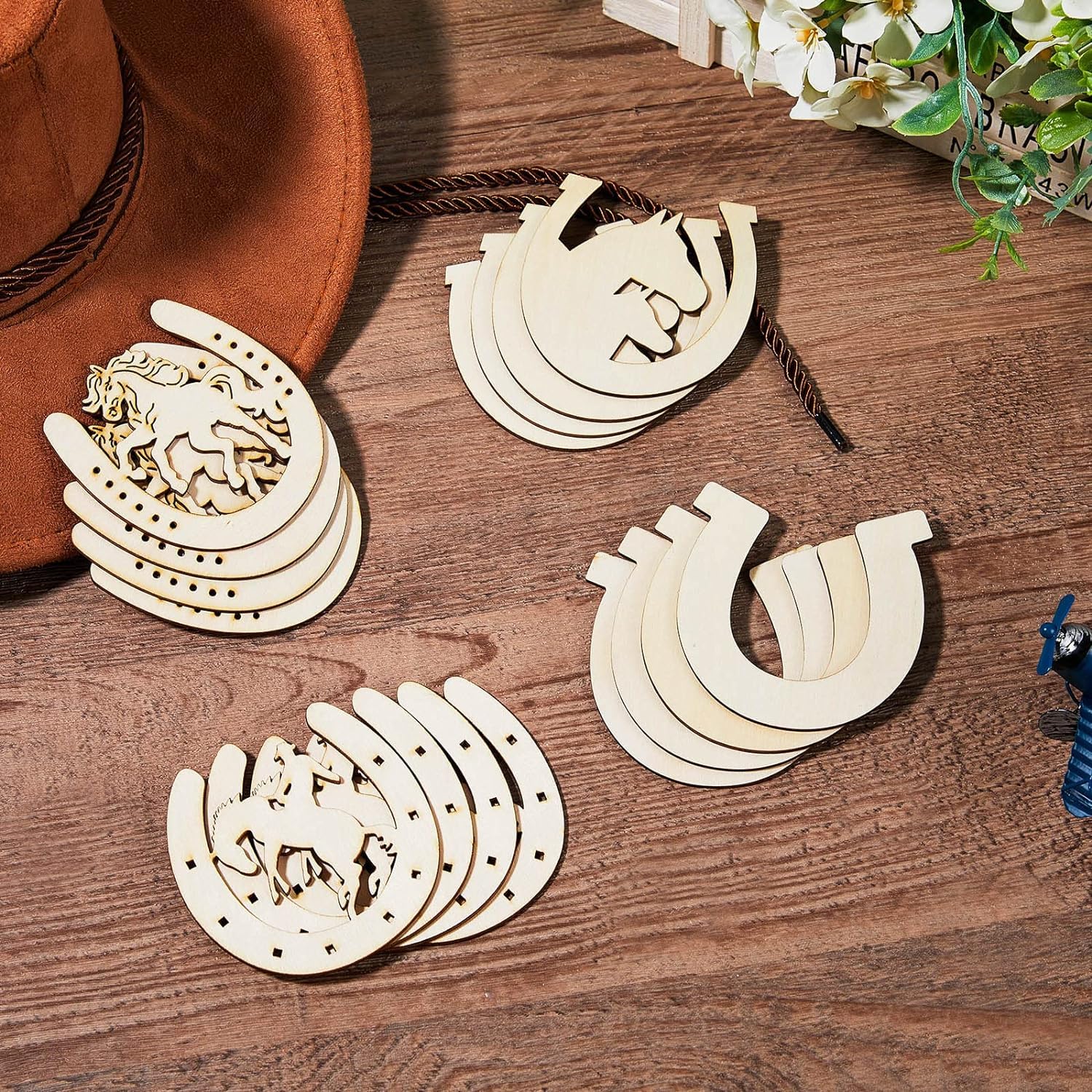 Wooden horse shoe decorations on a wooden surface with a hat and flowers in the background.
