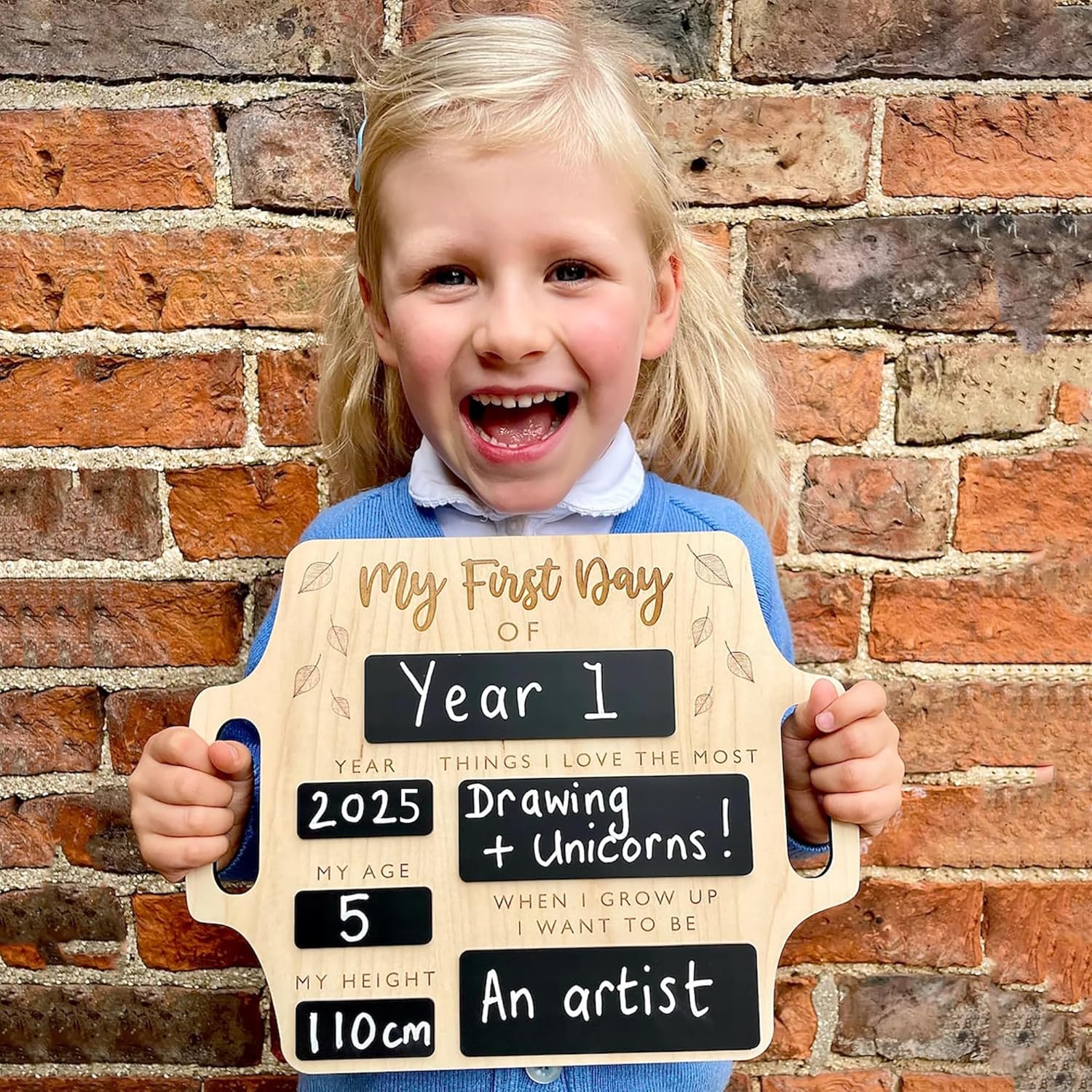 Child holding a sign with 'My First Day of Year 1' and personal information against a brick wall.