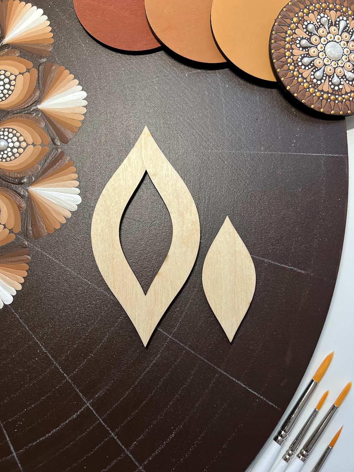 Wooden earring shapes on a dark surface with color swatches and paintbrushes.