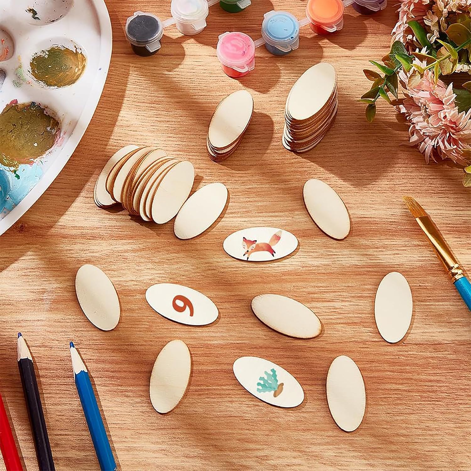 Wooden oval shapes with painted designs on a wooden table with art supplies.