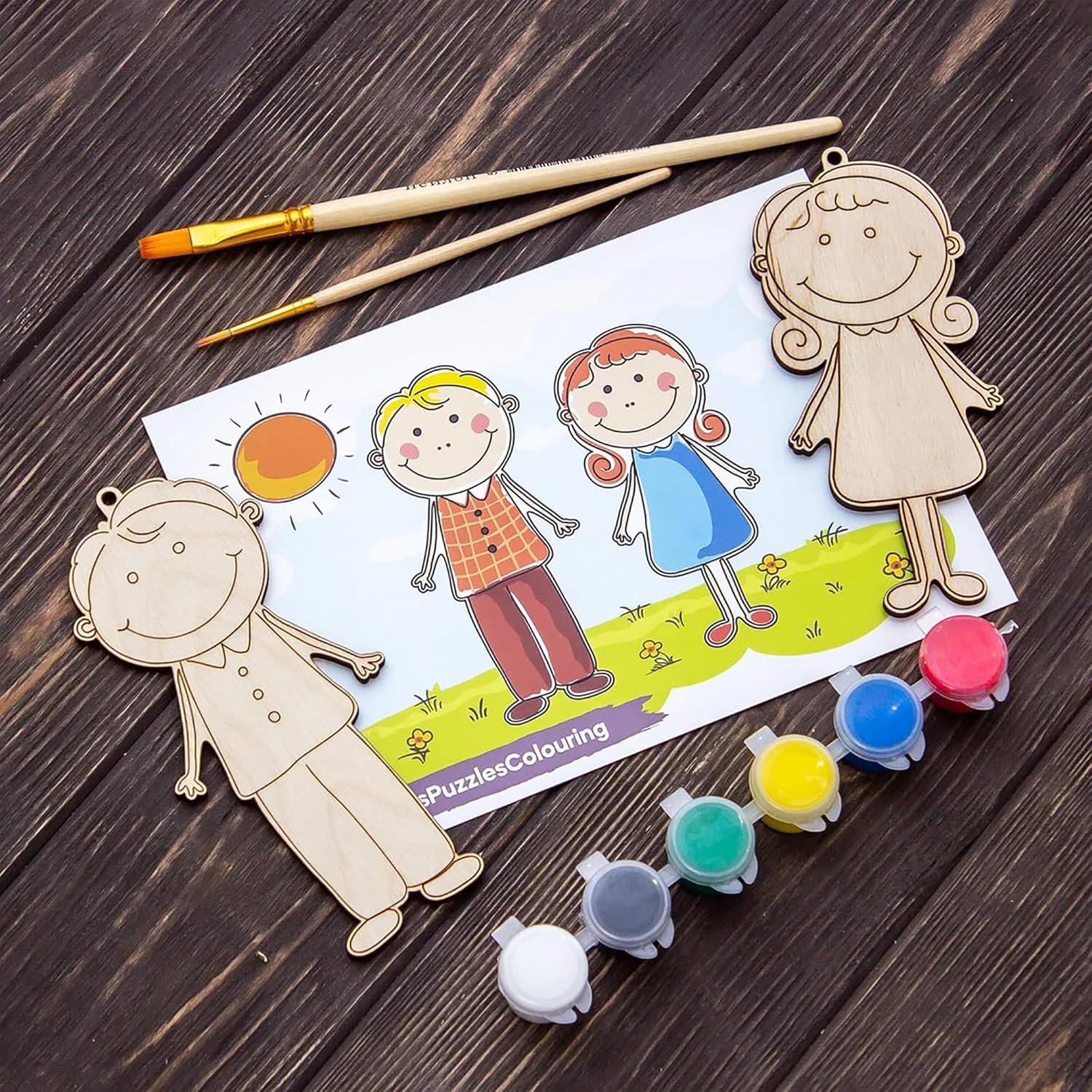Wooden cutouts of children and a sun, with paint bottles and brushes on a wooden surface.