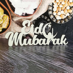 Wooden 'Eid Mubarak' sign on a dark surface with food items in the background