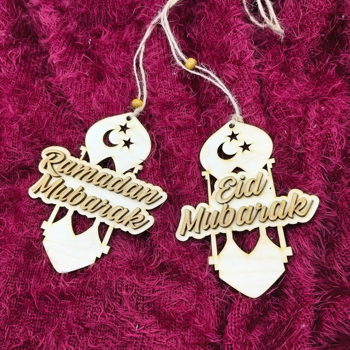 Decorative hanging tags with 'Ramadan Mubarak' and 'Eid Mubarak' text on a textured pink background.