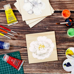 Art supplies including paint, brushes, and a partially completed white flower painting on a wooden surface.