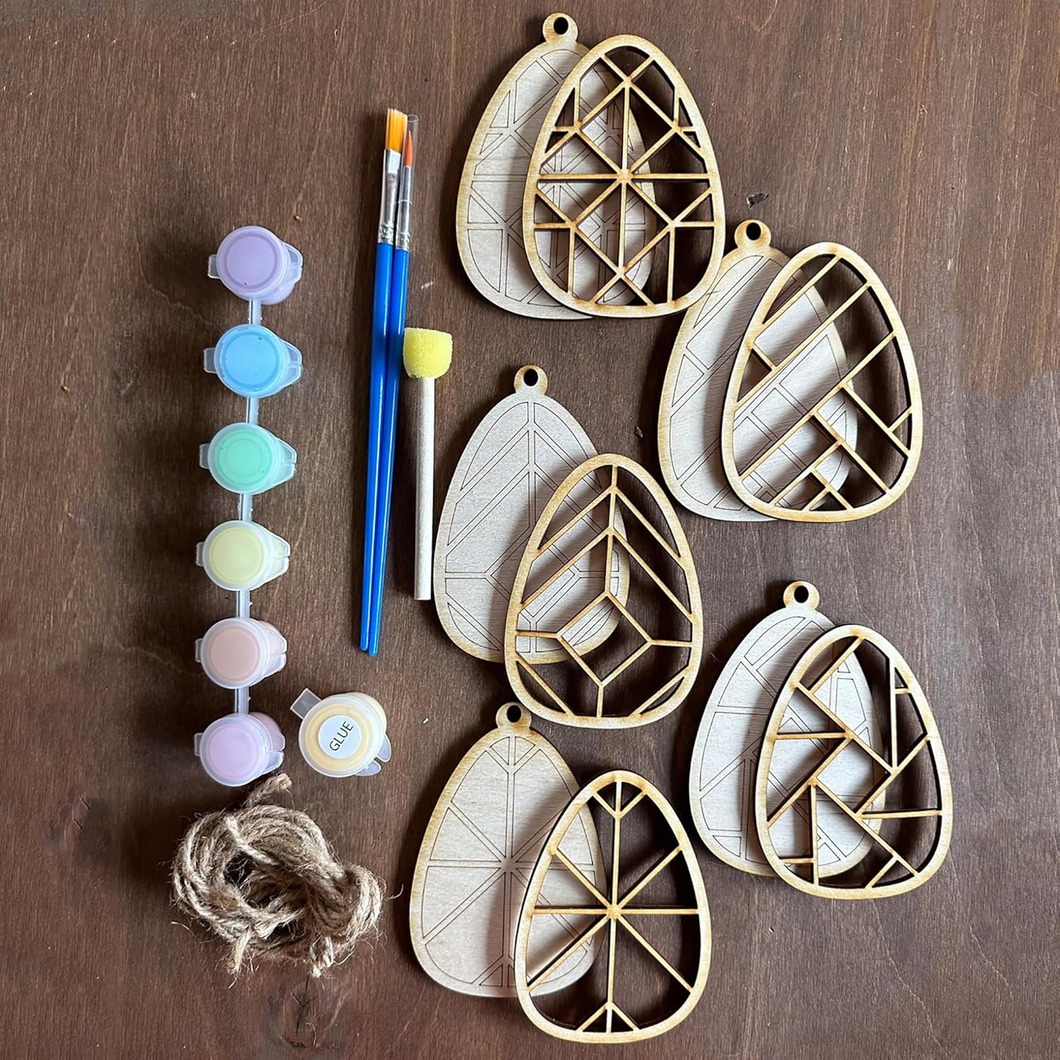 Geometric wooden wall hangings with paintbrushes, paint, and twine on a wooden surface