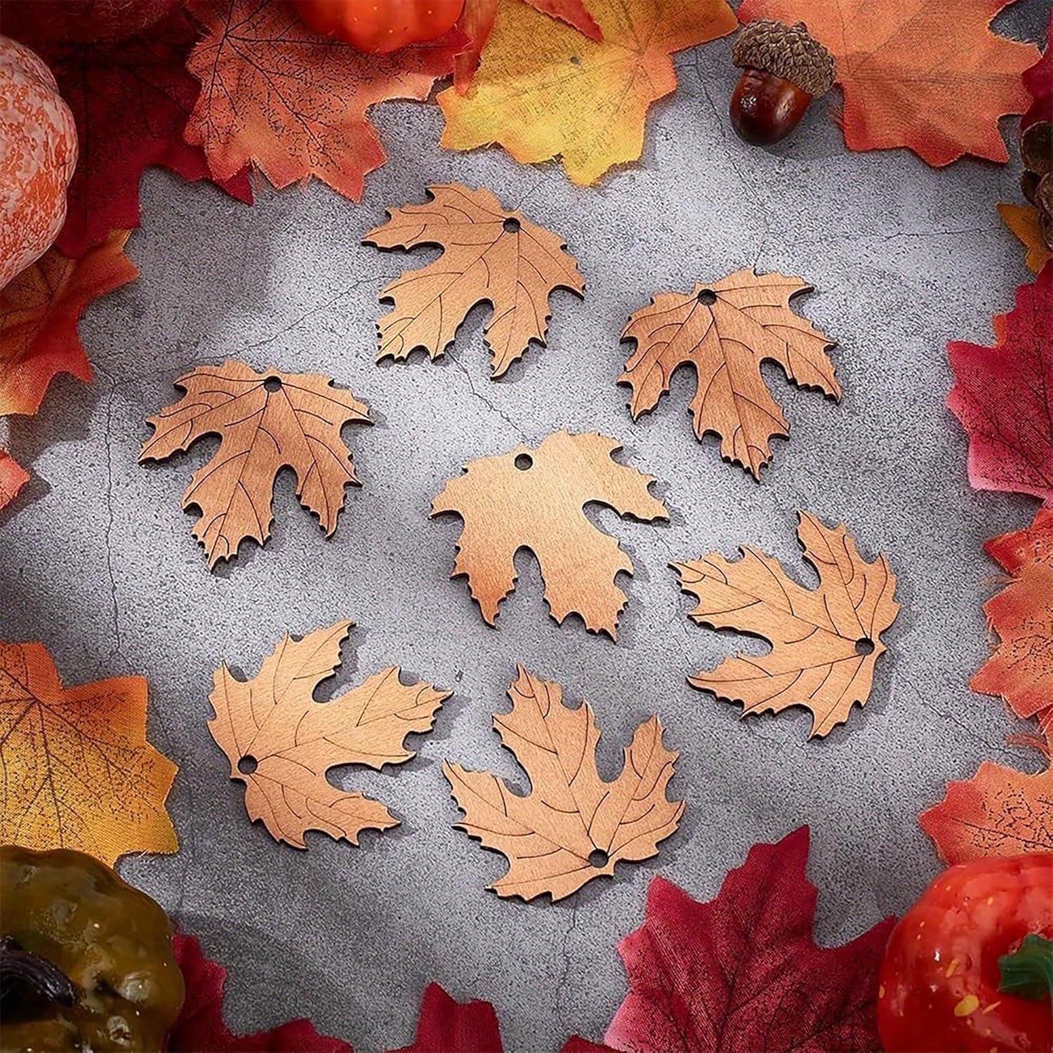 Decorative leaf-shaped ornaments on a textured surface with autumn leaves and acorns.