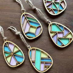 Geometrically patterned teal, purple, and gold hanging decorations on a wooden surface.