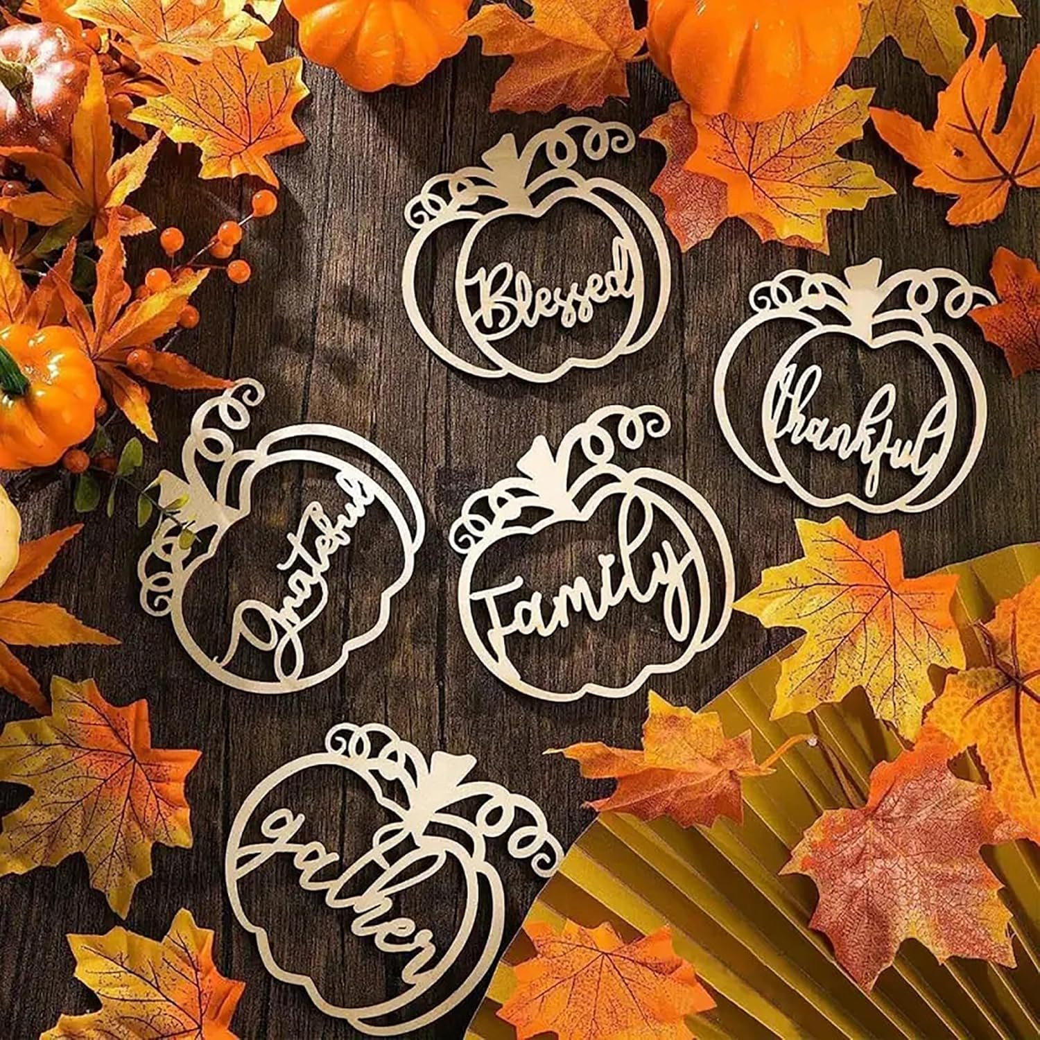 Decorative pumpkin-shaped cutouts with Thanksgiving phrases on a wooden surface with fall leaves.