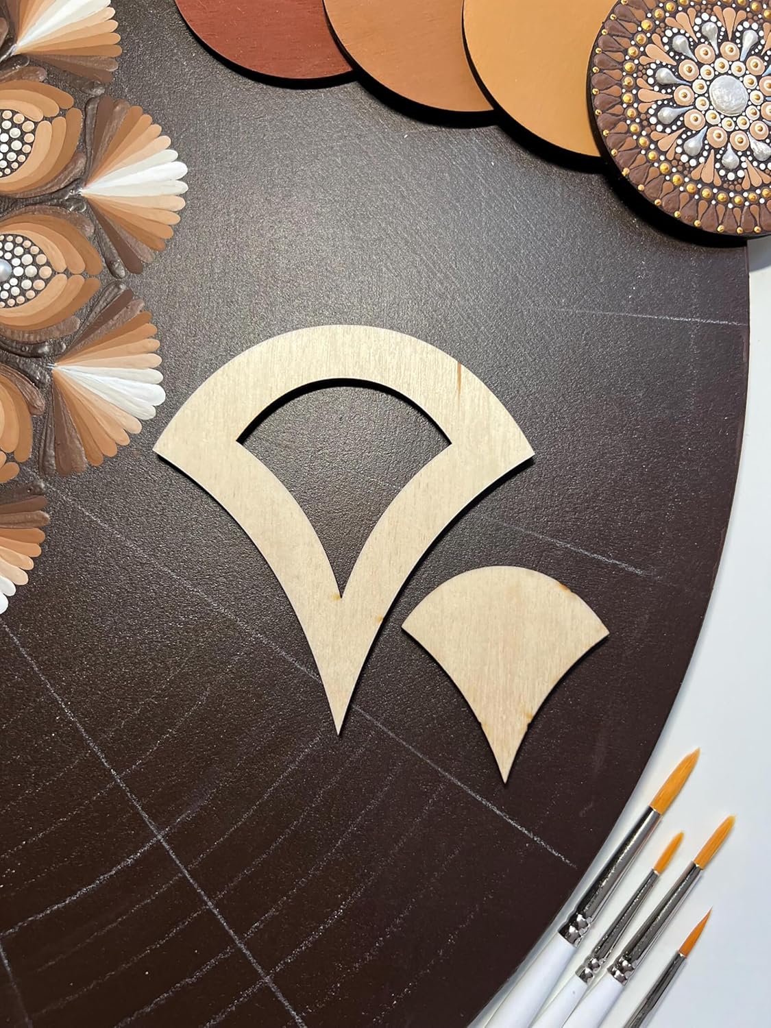 Wooden cutouts of a decorative design on a dark surface with paintbrushes.