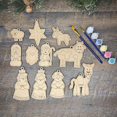 Set of wooden nativity scene ornaments on a wooden surface with paintbrushes and paint.