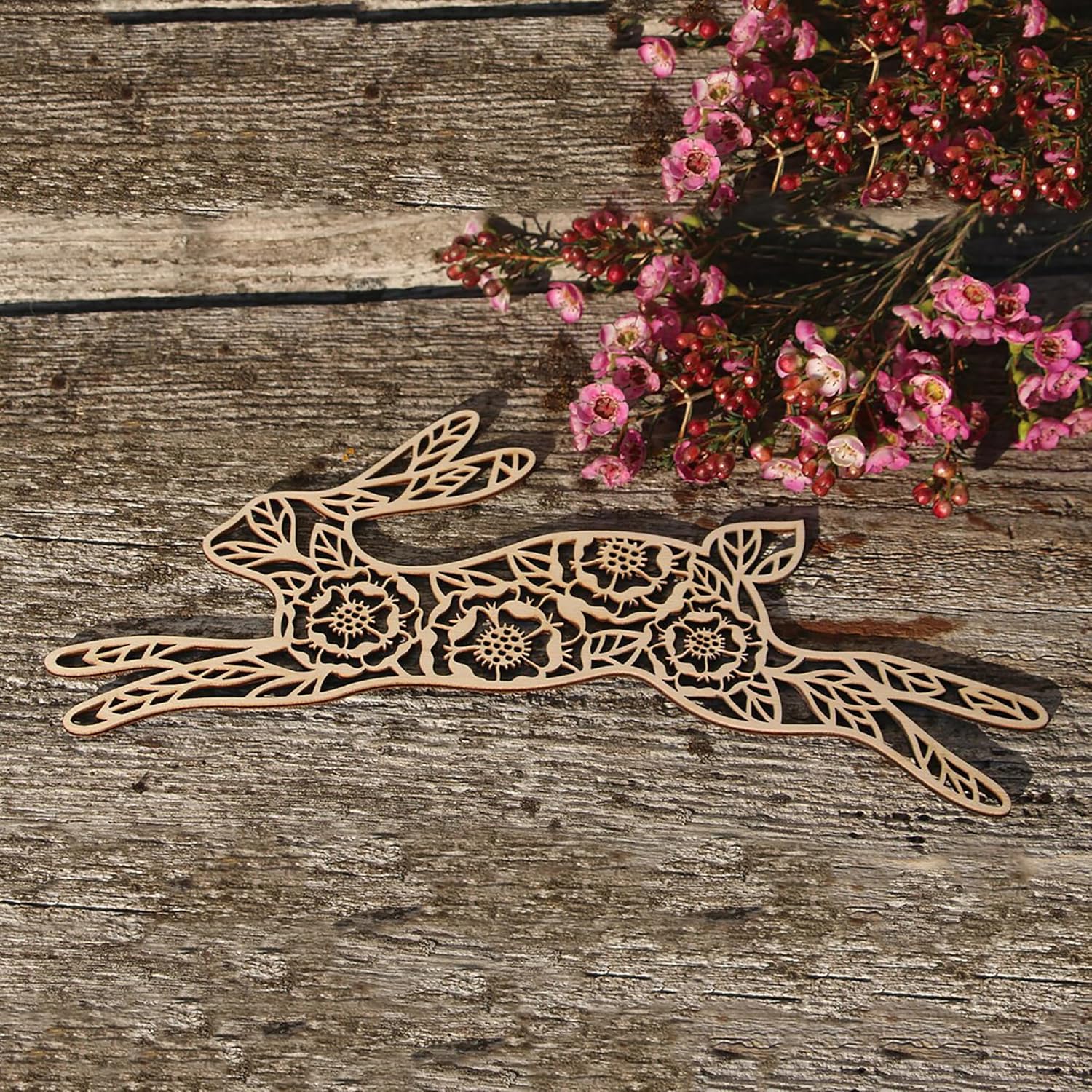 Decorative wooden hare with floral patterns on a rustic wooden surface with pink flowers.