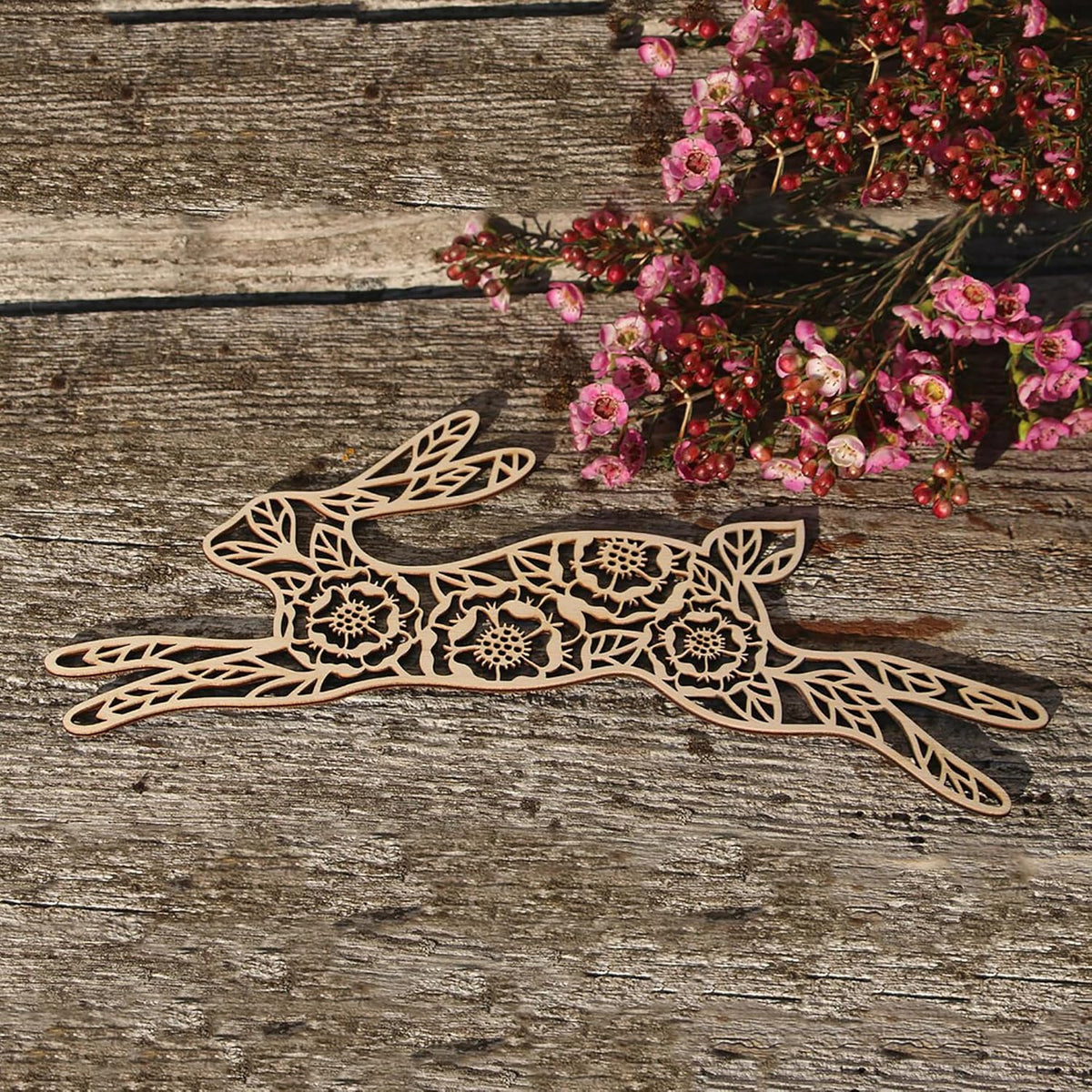 Decorative wooden hare with floral patterns on a rustic wooden surface with pink flowers.